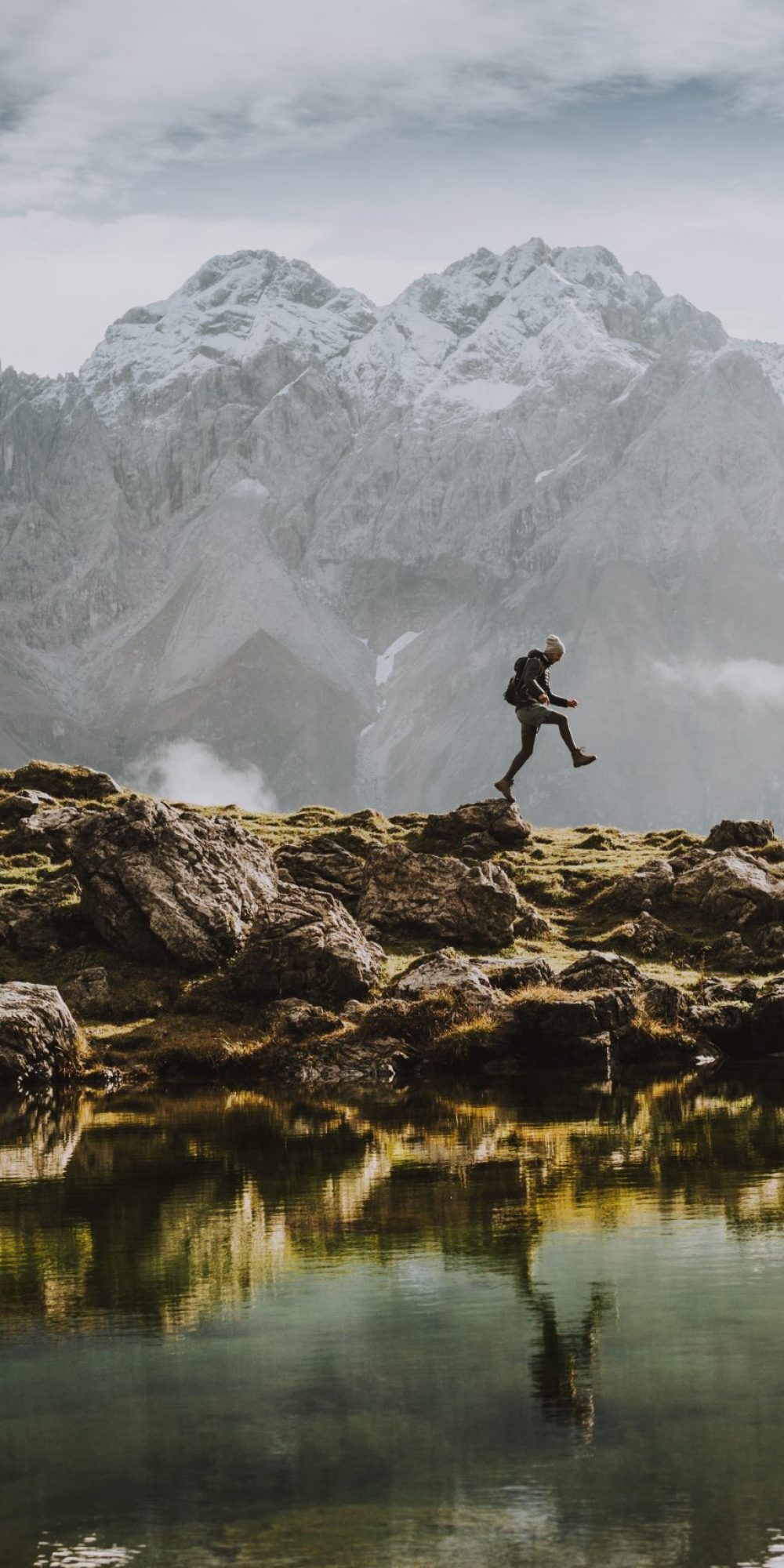 Ein einsamer Wanderer springt an einem Bergsee über Steine
